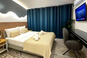Dormitorio moderno con cortinas azules, silla gris y televisión en pared