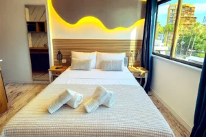 Cama de matrimonio confortable con toallas limpias y ventana soleada