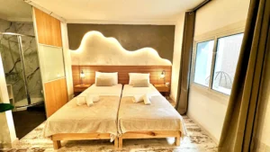 Vista frontal del dormitorio doble con cabecero iluminado y cortinas